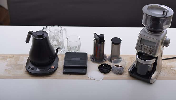 A neatly organized flat-lay photo of essential gear required for inverted brewing is presented. This includes the AeroPress brewer, timer, filters, grinder, kettle, measuring tools, and a mug. 